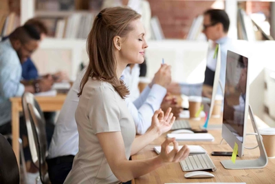 Woman meditating at desk in busy office